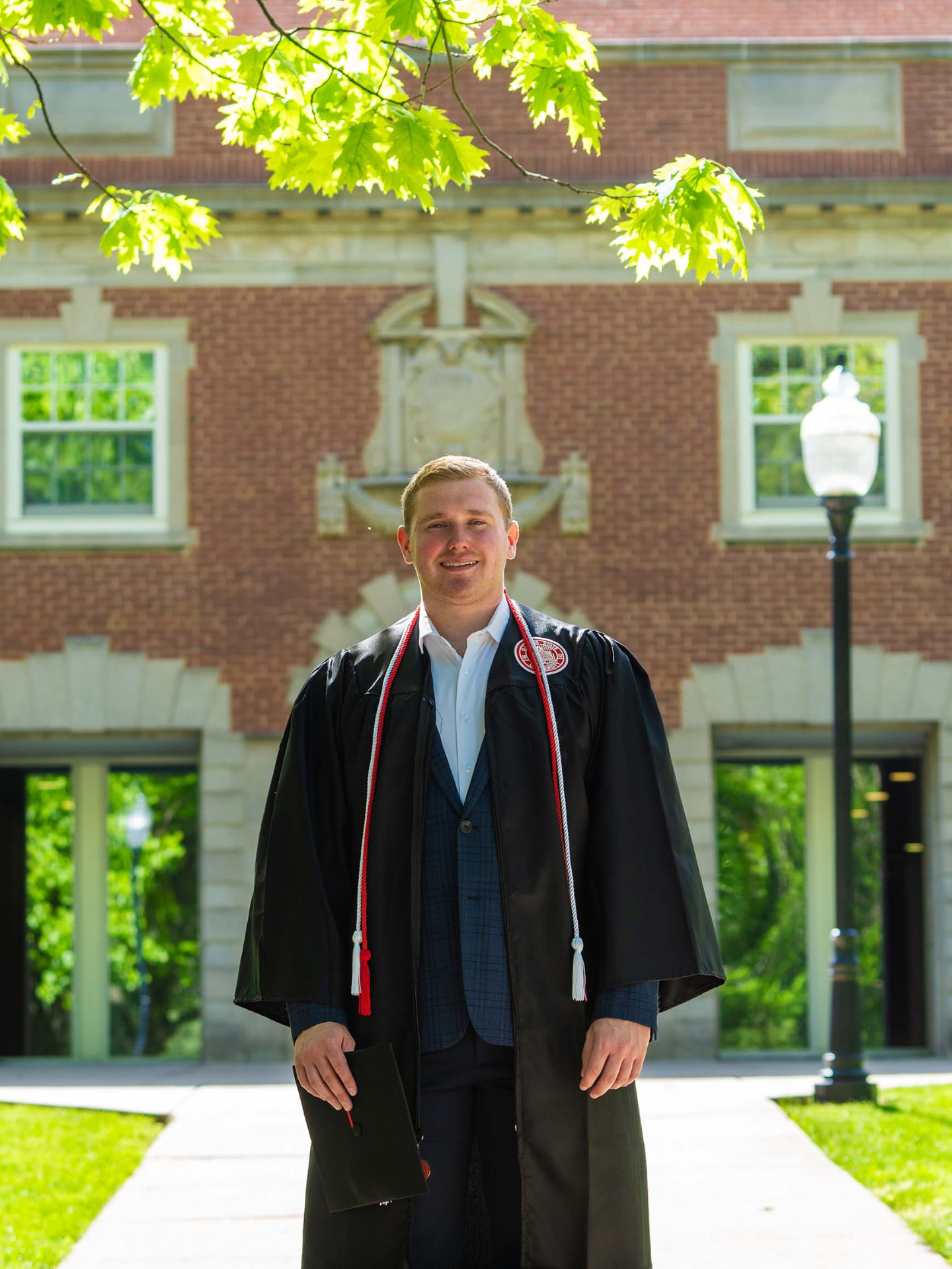 Graduate in cap and gown outside a brick campus building