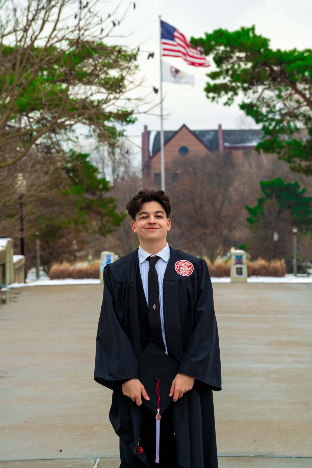 Graduate in cap and gown on the quad with the flagpole behind him