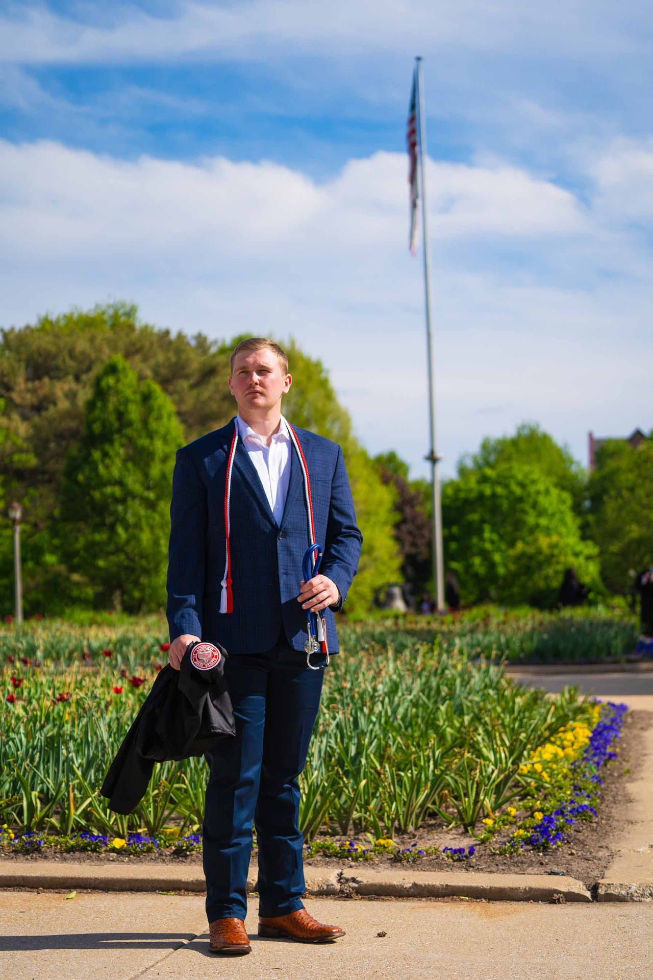 Graduate in a blue suit with honor cords by the campus tulip beds