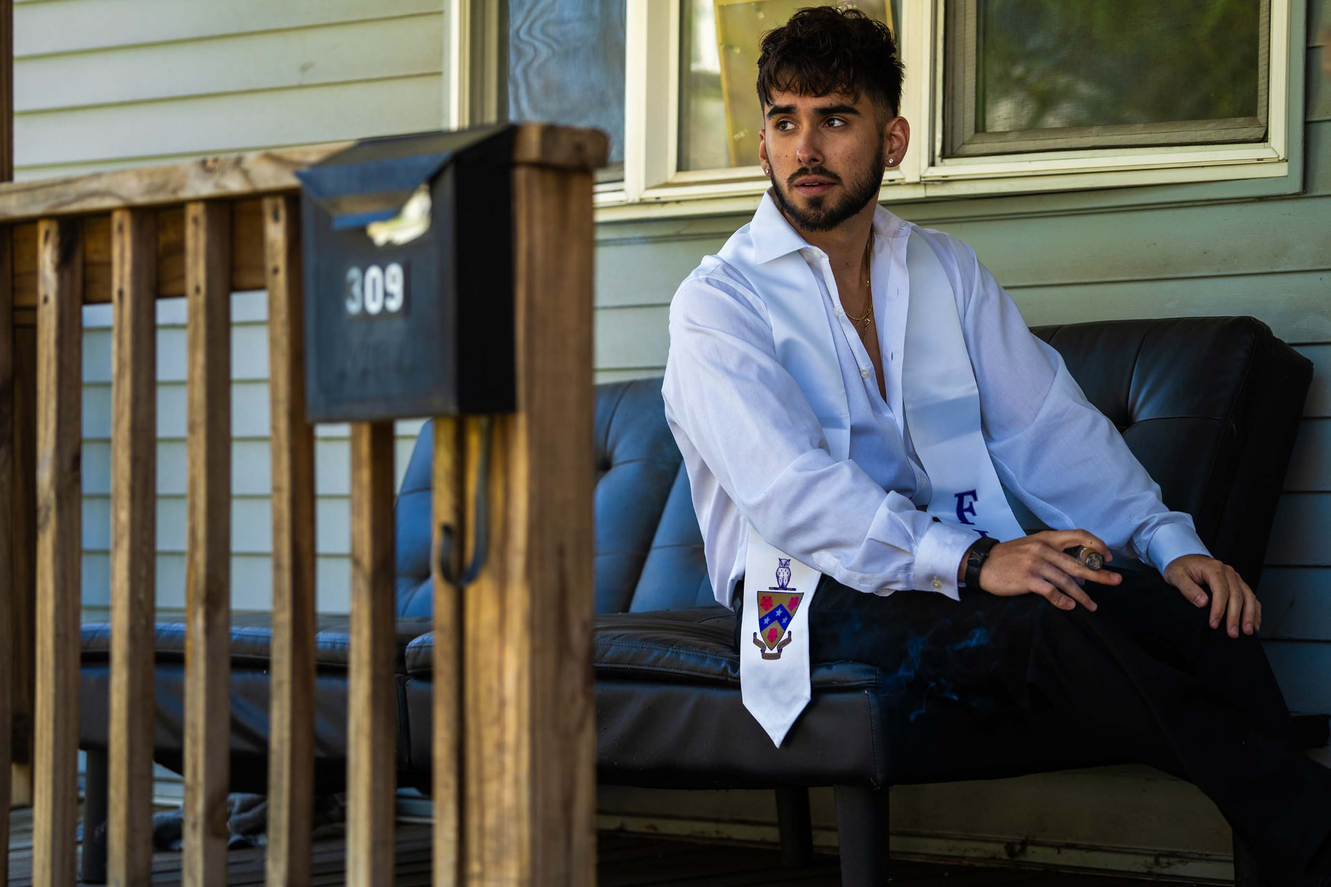 Graduate in a white shirt and stole smoking a cigar on a front porch