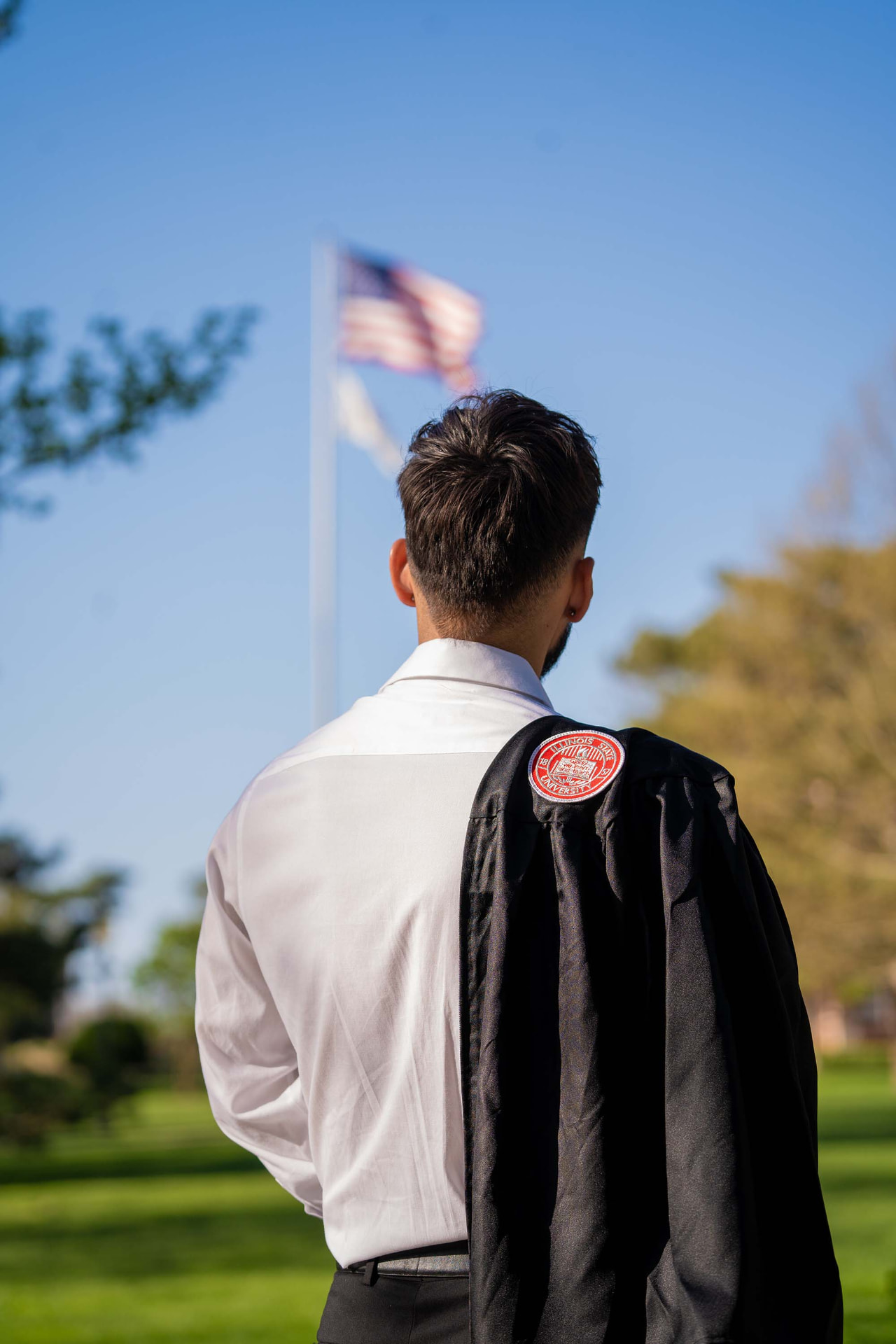 Graduate looking toward the flag with his gown over his shoulder